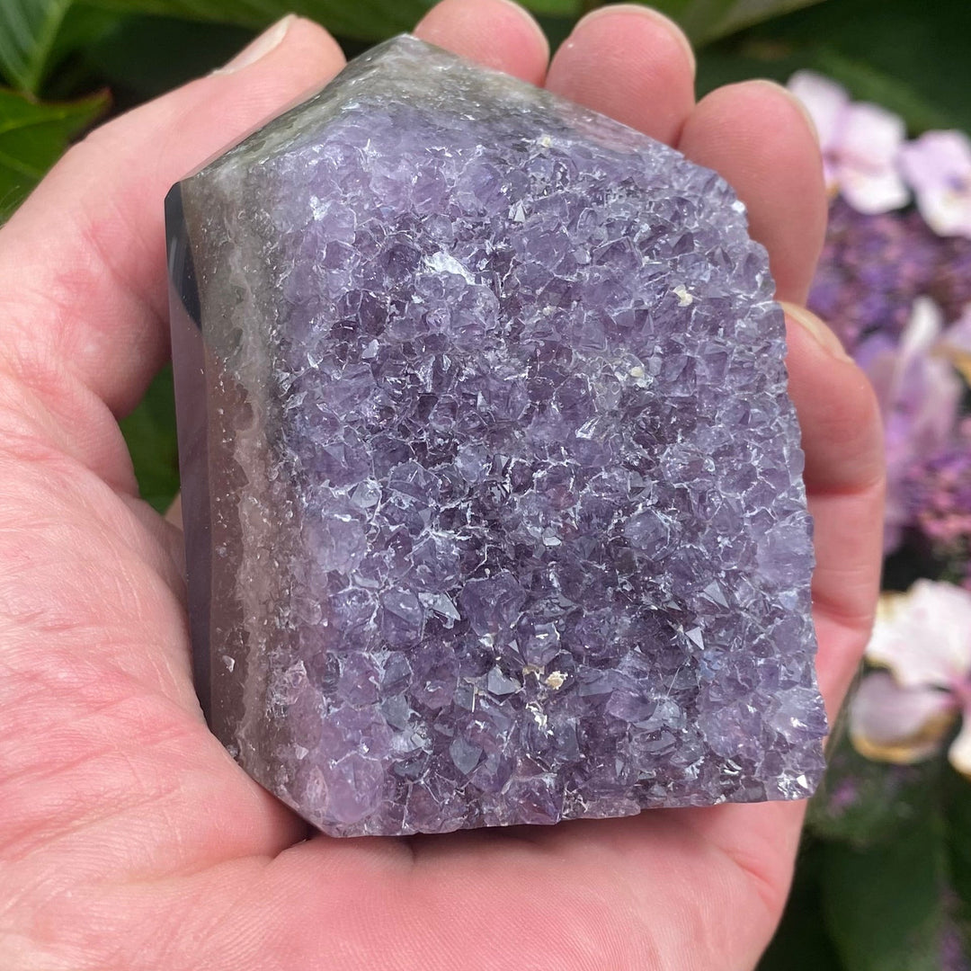 A Chunky Amethyst Point held in a hand in a garden on a bright sunny day