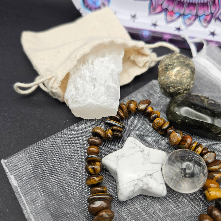 A crystal and gemstone set arranged on a dark surface, including a white quartz cluster with a cream drawstring pouch, a beaded bracelet with brown tiger&
