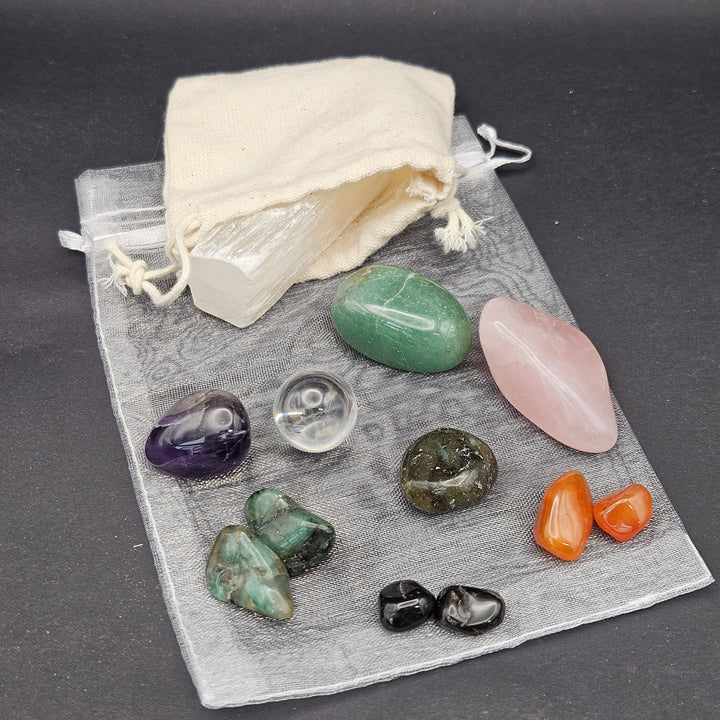 A set of polished and tumbled crystals displayed on a sheer white drawstring pouch with a white fabric bag, arranged on a dark gray background. 