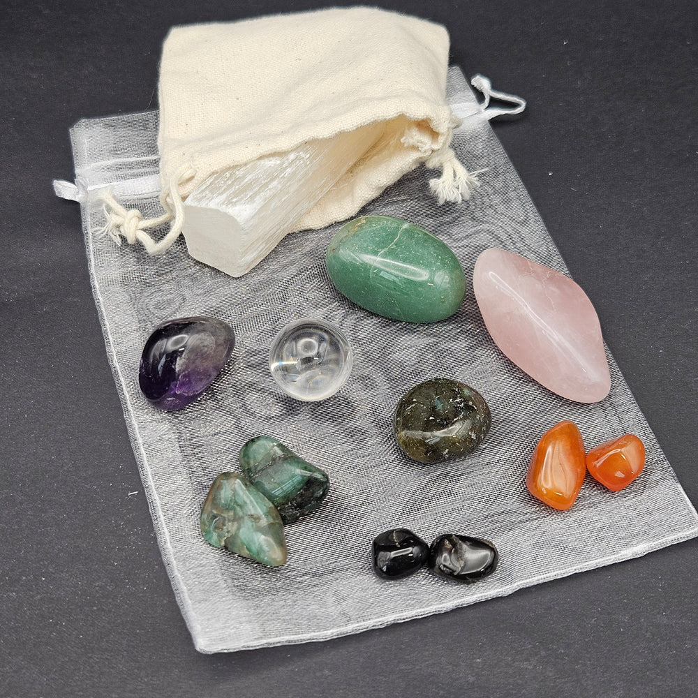A set of polished tumbled crystals and stones displayed on a sheer gray drawstring pouch with an off-white fabric pouch, arranged on a dark gray background. 