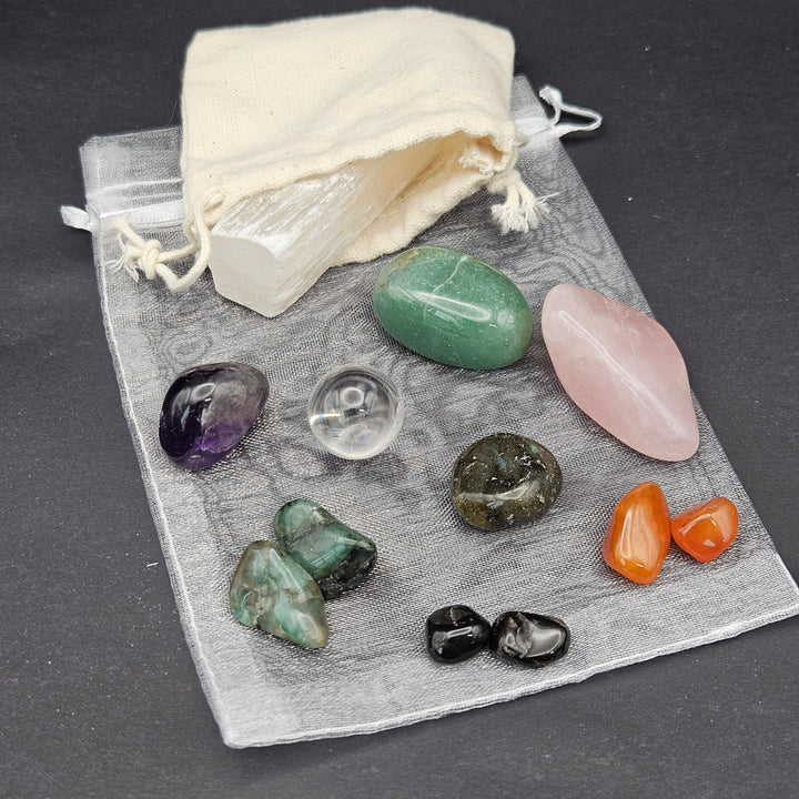 A set of polished tumbled crystals and stones displayed on a sheer gray drawstring pouch with an off-white fabric pouch, arranged on a dark gray background. 