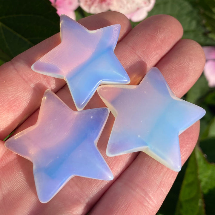3 Opalite Star Crystal Carvings held in a hand in a garden on a bright sunny day