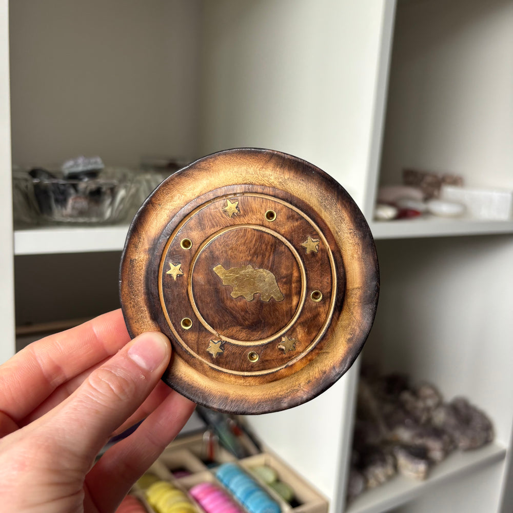 Hand holding a wooden and brass decorative item with a bear design.