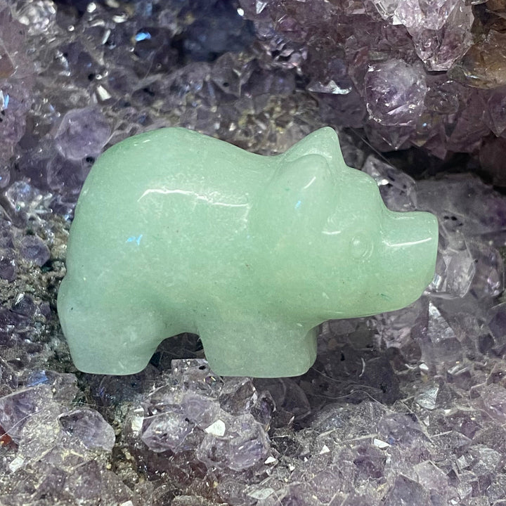 A small Green Aventurine Pig Carving displayed on a bed of purple and clear crystal points.