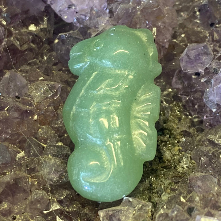 A small Green Aventurine Seahorse Carving displayed on a purple amethyst crystal cluster.