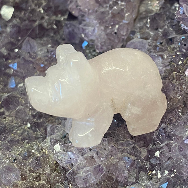 A small Rose Quartz Pig Carving placed on a textured purple crystal cluster background.