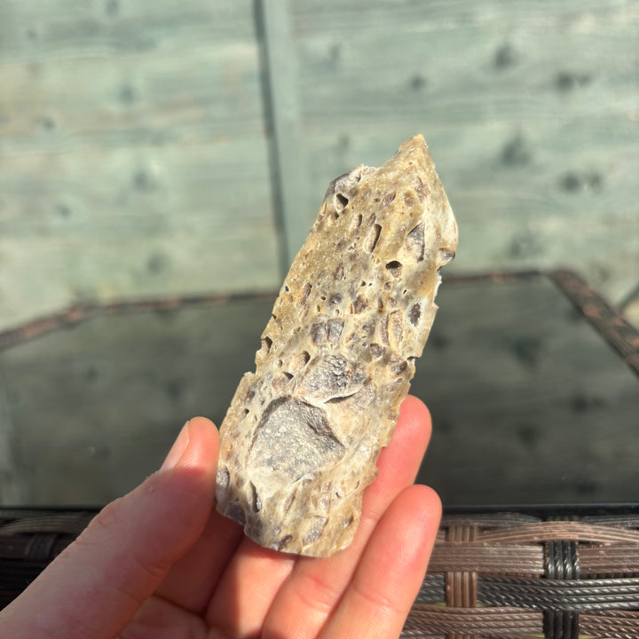 A sphalerite crystal tower held in front of a reflective surface with a wooden background.