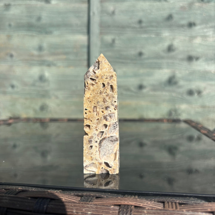 A sphalerite crystal tower displayed on a reflective surface with a wooden background.