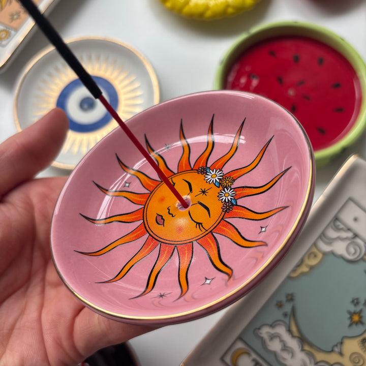 Small pink dish with a sun design held by a hand, surrounded by other decorative items.