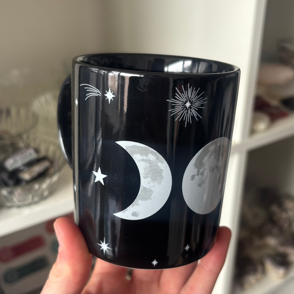 Black mug with moon and star design held by a hand against a blurred indoor background