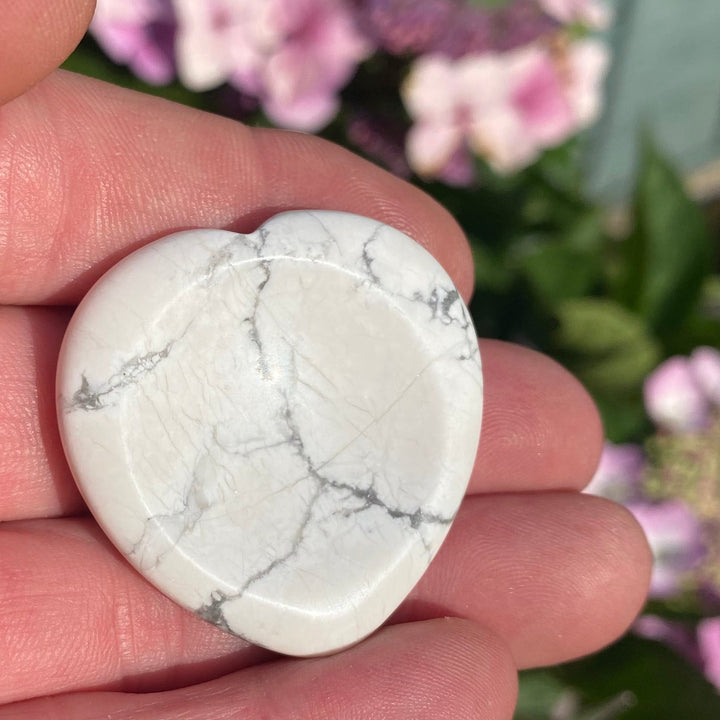 A heart-shaped Howlite crystal with gray veining, held in a person&