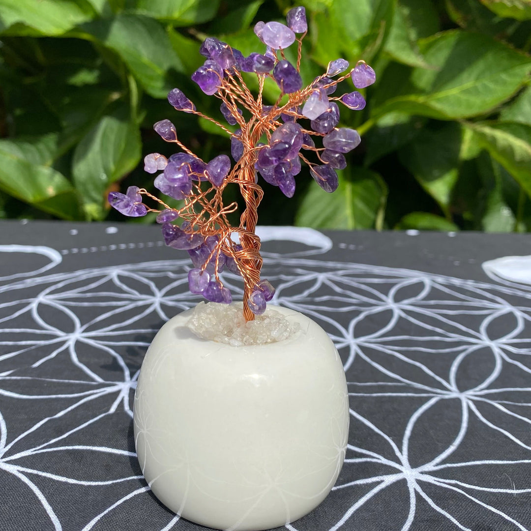 Handmade Amethyst crystal tree with deep purple gemstone leaves on flexible wire branches, set in a smooth round quartz base, shown in a close-up outdoor setting.