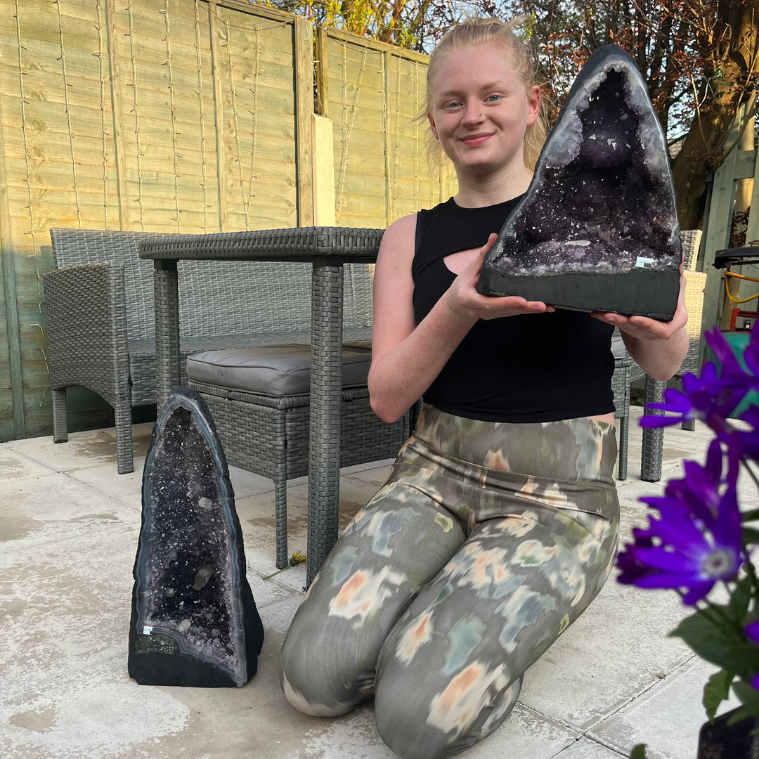 A person kneeling to display two large amethyst crystal pieces on a patio.  #style_tall 