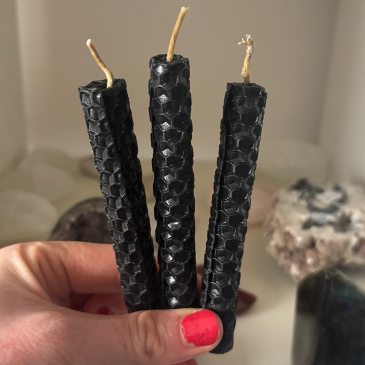 Hand holding three black textured candles with a blurred background