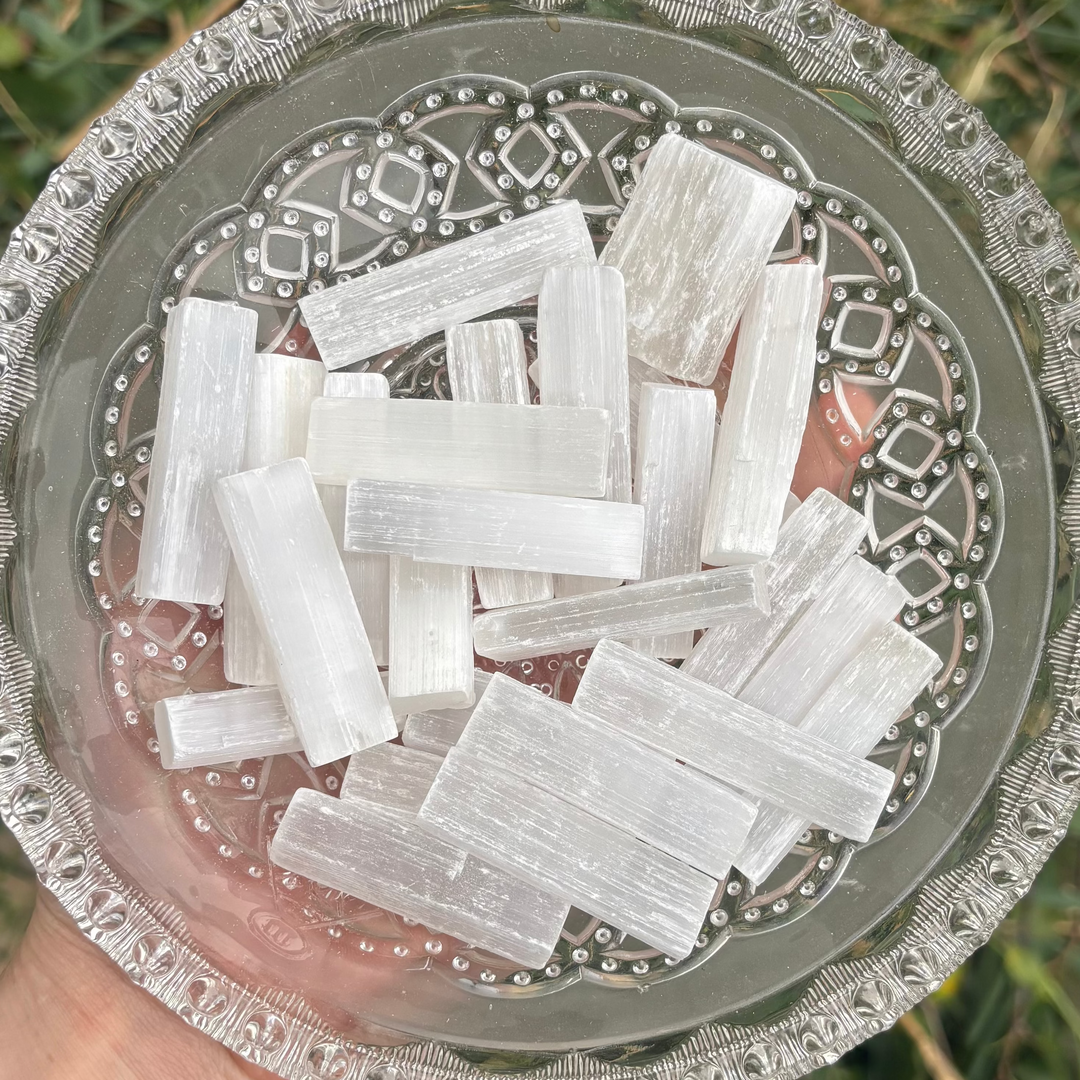 Clear glass bowl filled with white Mini Selenite Sticks held over a natural background