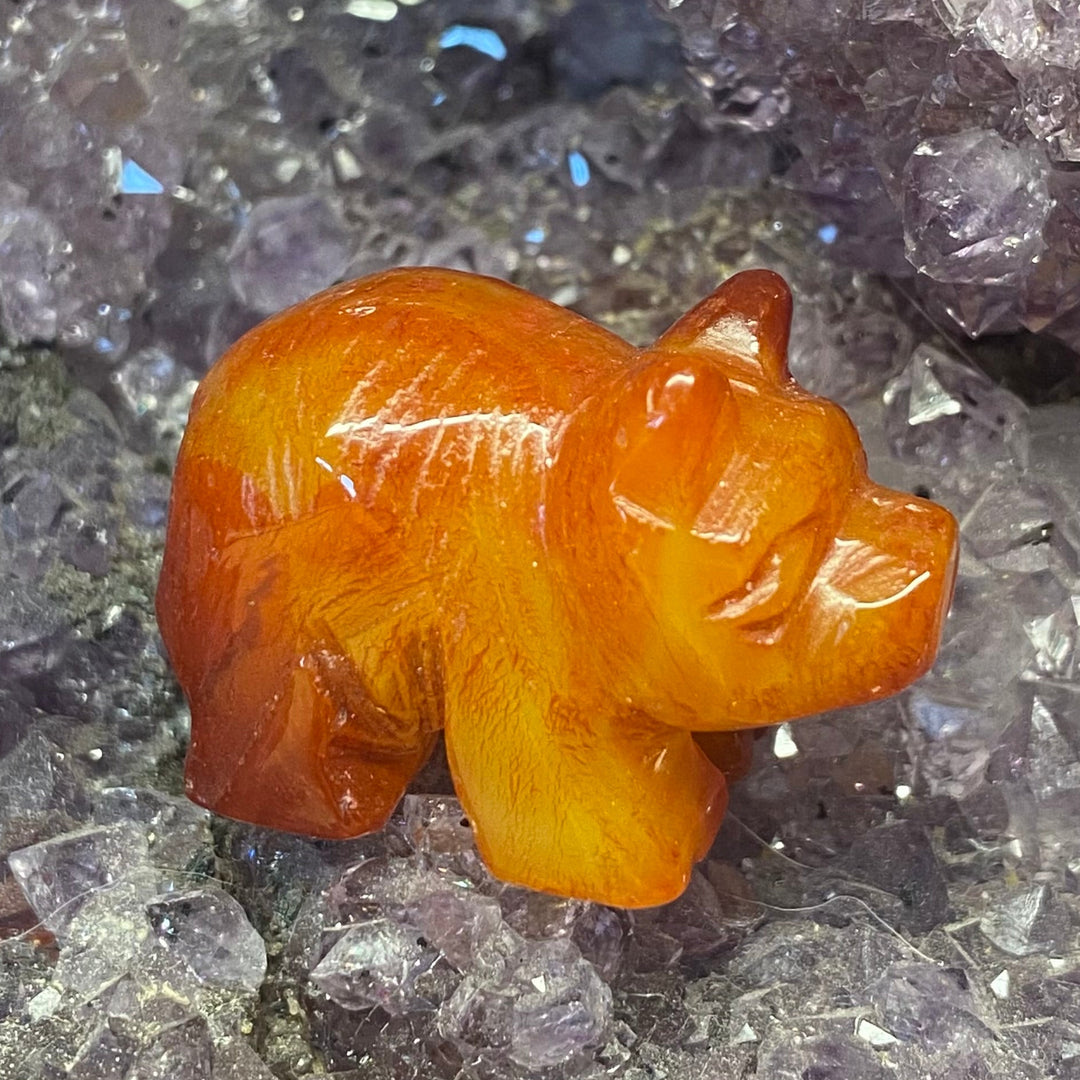 A small carved Carnelian Pig Carving displayed on a textured purple crystal cluster background.