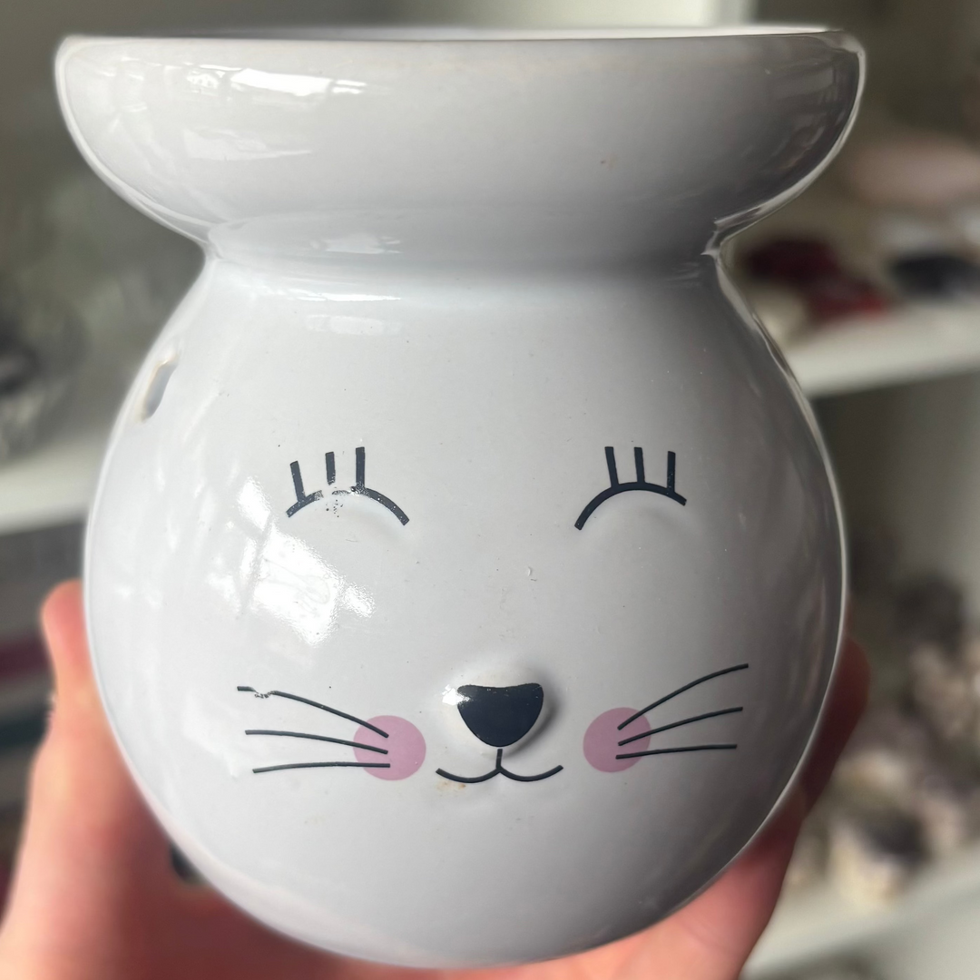 White ceramic diffuser with a cat face design held in a hand against a blurred indoor background