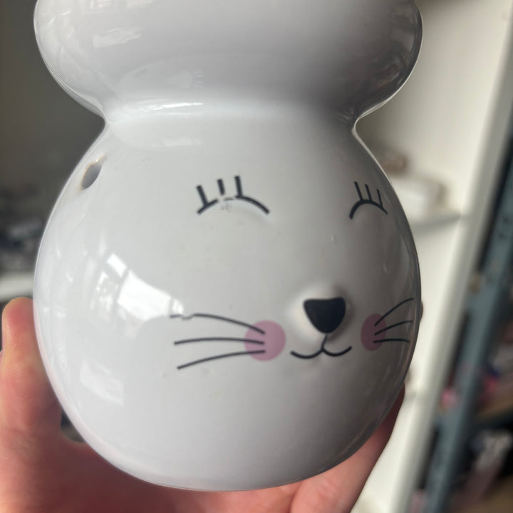 White ceramic cat-shaped object with a face design held in a hand.