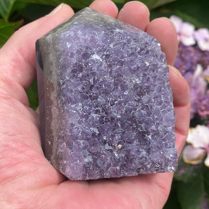 A Chunky Amethyst Point held in a hand in a garden on a bright sunny day