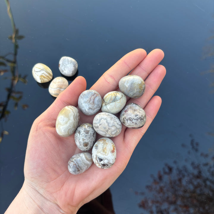 A hand holding several polished agate stone pendants with natural banded patterns in shades of gray, white, beige, and brown, set against a dark blue background.