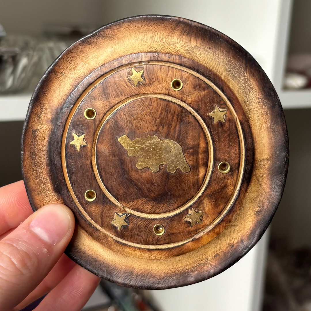 Hand holding a wooden and brass decorative item with a bear design.
