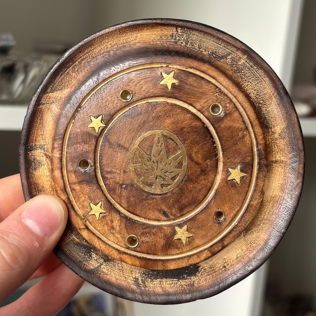 Wooden coaster with star and leaf design held by a hand in front of a shelf.