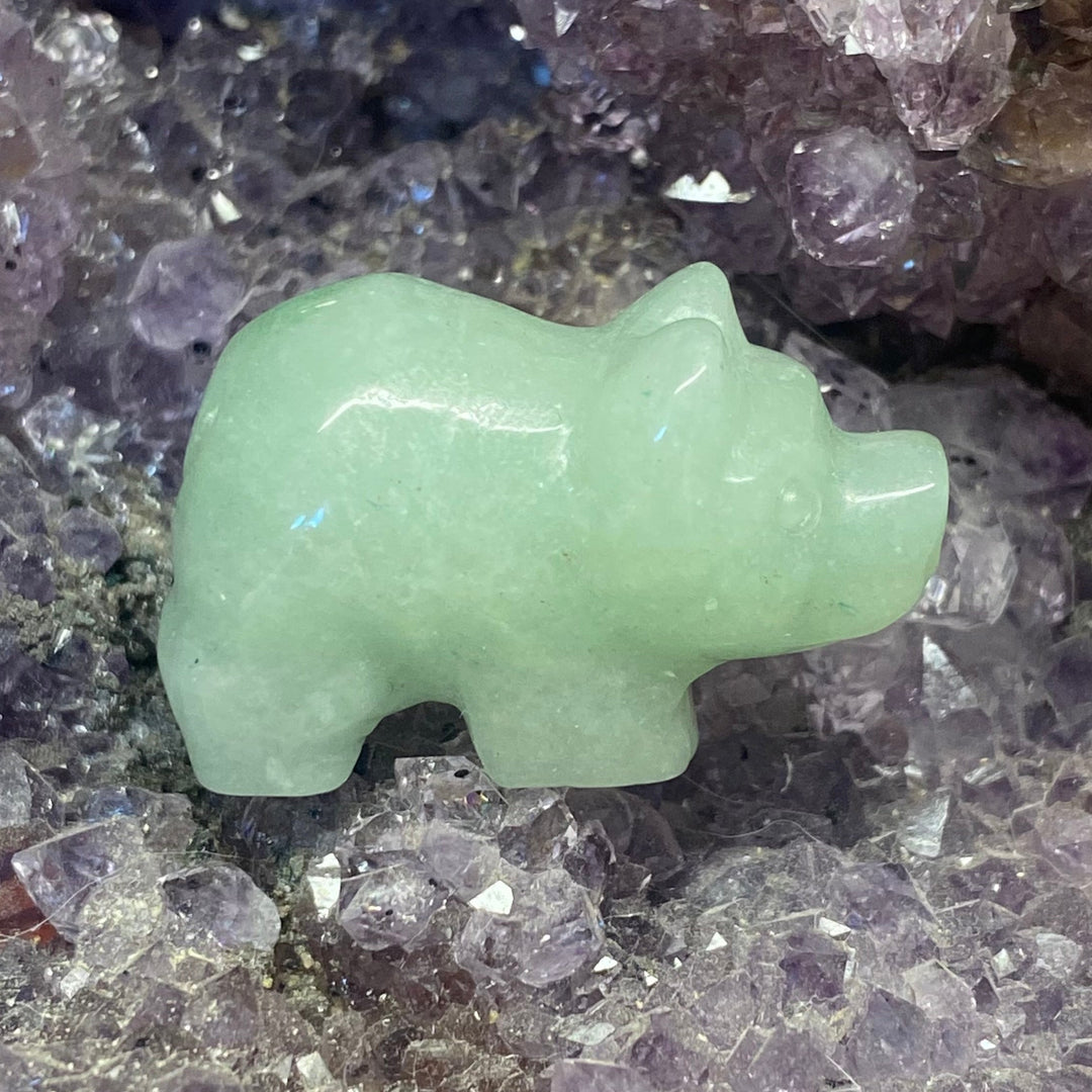 A small carved green stone pig figurine resting on a purple crystal geode matrix.