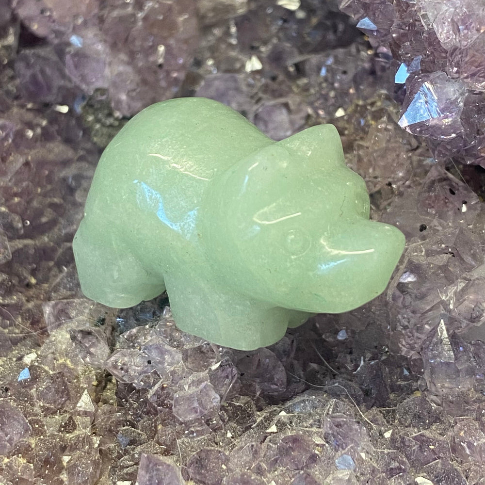 A small carved green stone pig, placed on a bed of purple crystal clusters.