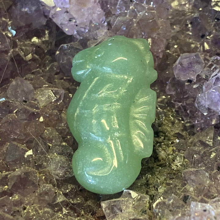 A small carved Green Aventurine Seahorse Carving placed on a bed of purple and clear crystals.
