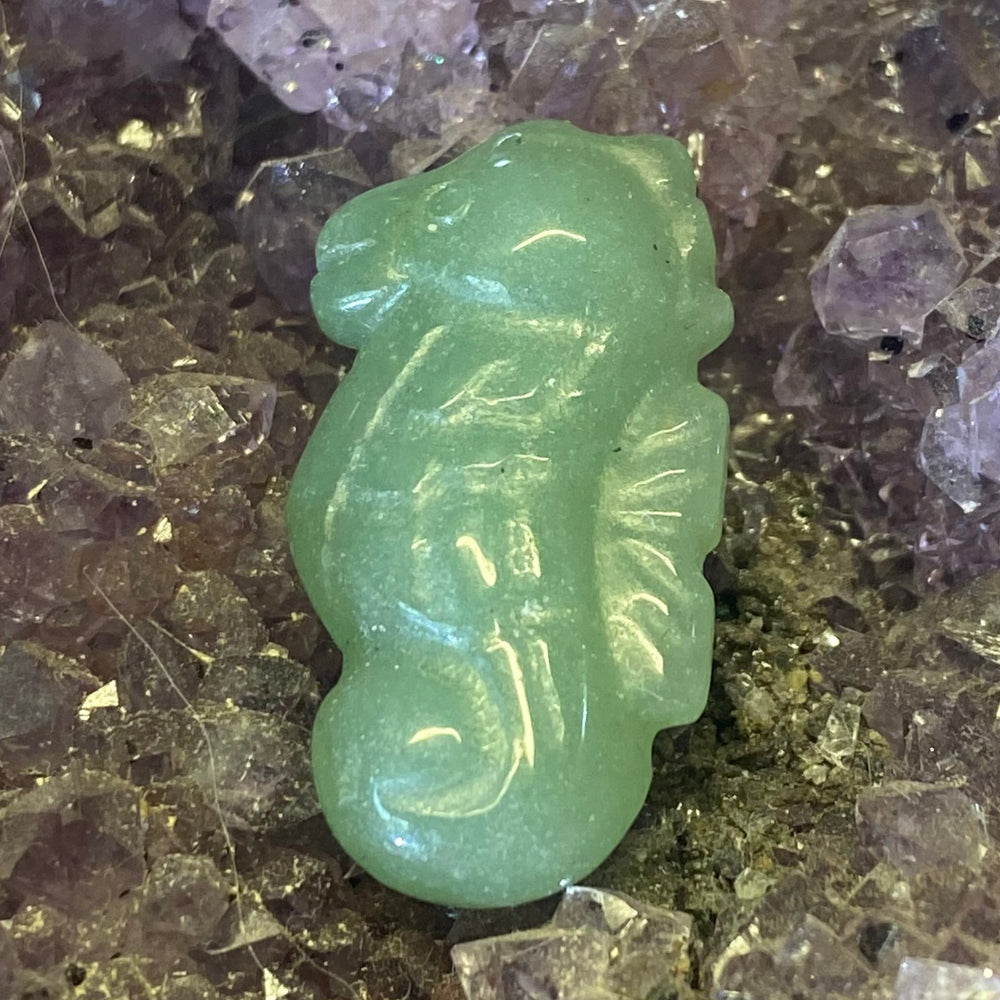 A small carved Green Aventurine Seahorse Carving displayed on a bed of purple and clear crystals.