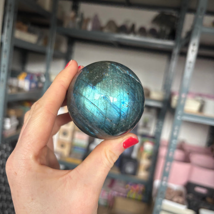 Hand holding a Labradorite crystal ball in front of a blurred store shelf.