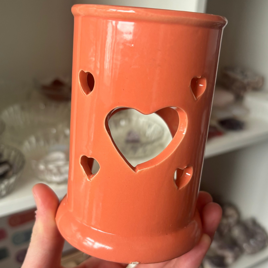 Hand holding an orange ceramic Heart Wax Melt Burner against a blurred indoor background