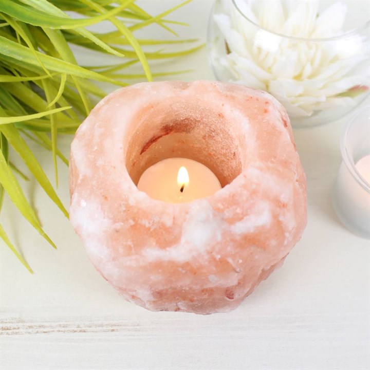 A Himalayan Salt Tea Light Holder with a burning candle on a plain white background with a plant next to it