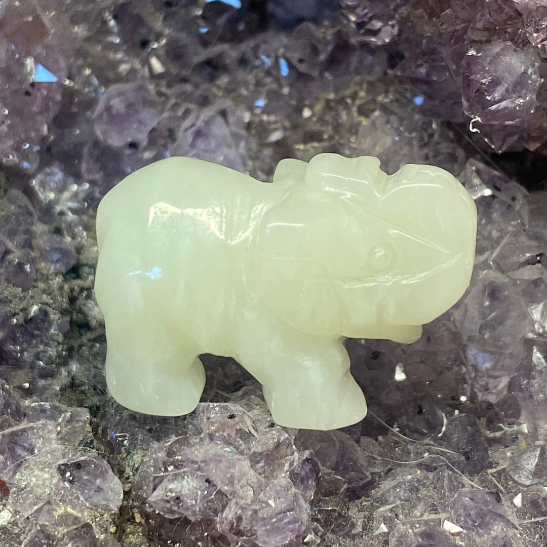 A small Jade Elephant Carving, placed on a bed of purple crystal points.