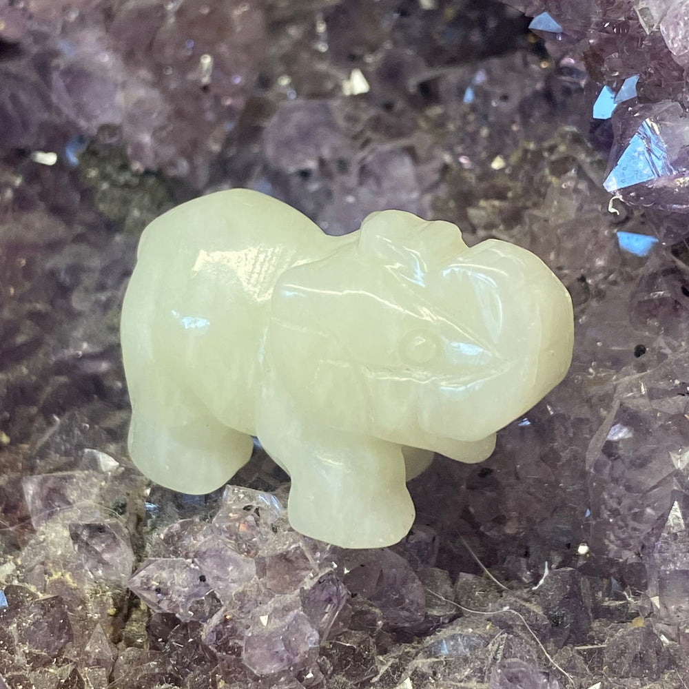 A small Jade Elephant Carving, placed on a bed of purple crystal points.