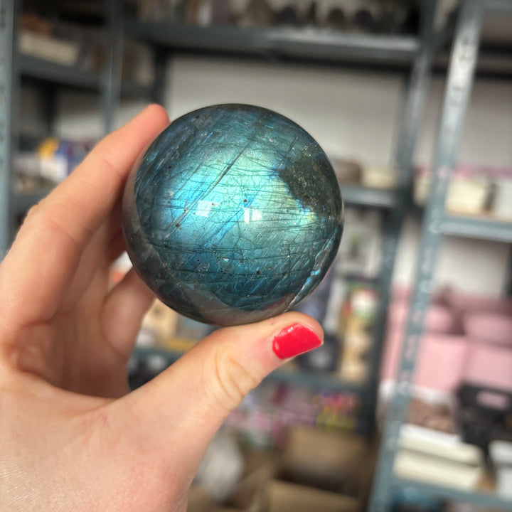 Hand holding a Labradorite Crystal Sphere crystal ball with a blurred indoor background