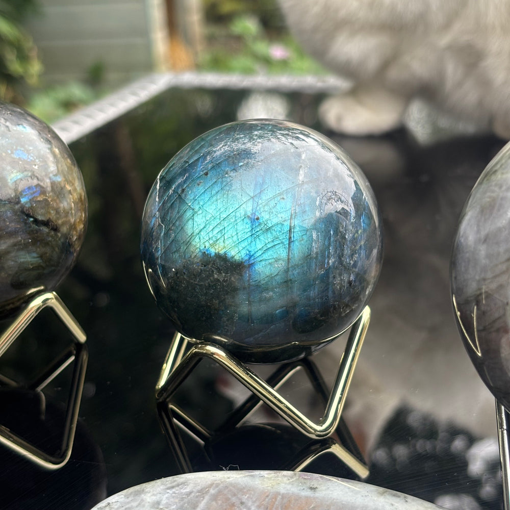 A polished labradorite crystal sphere with a blue iridescent flash, displayed on a gold metal stand.