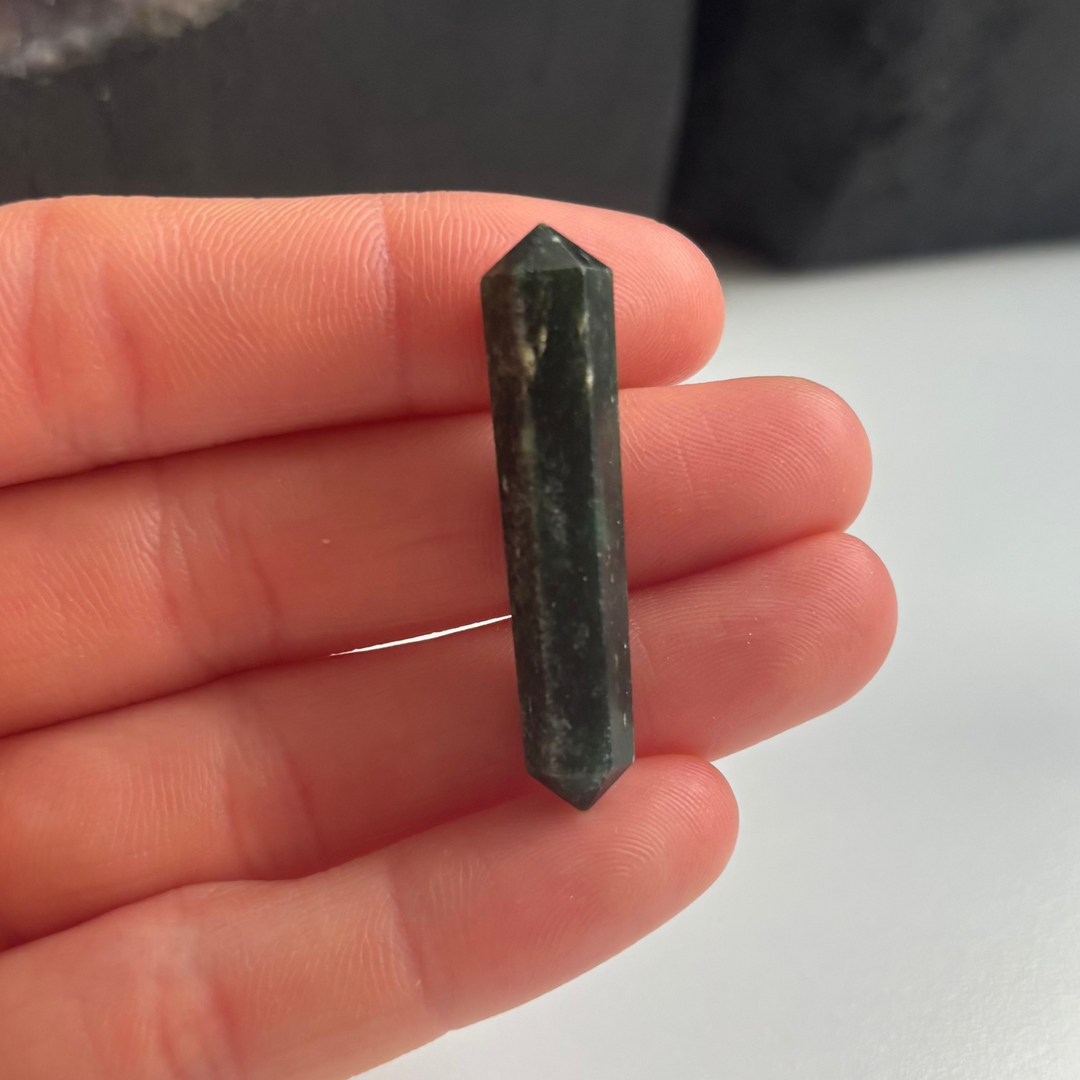 A hand holding a small green Tree Agate double-terminated point crystal with minor imperfections.