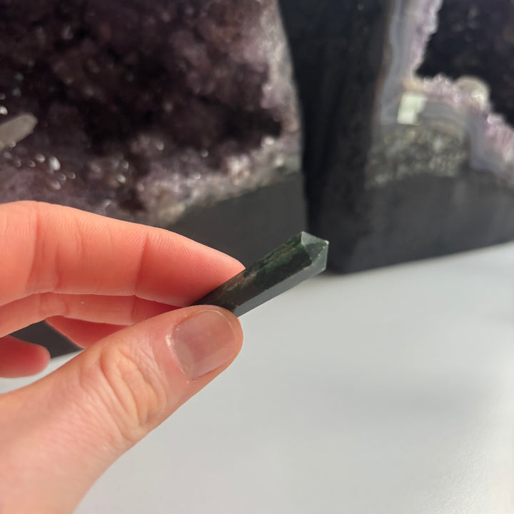 A hand holding a small green Tree Agate double-terminated Point.