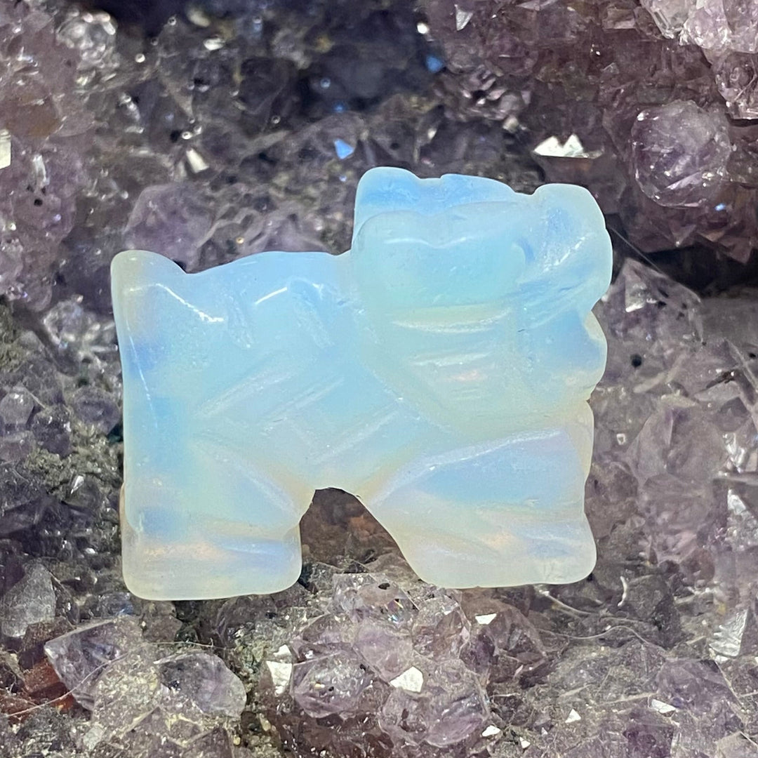 A small Opalite Dragon Carving, displayed on a bed of purple crystal points.