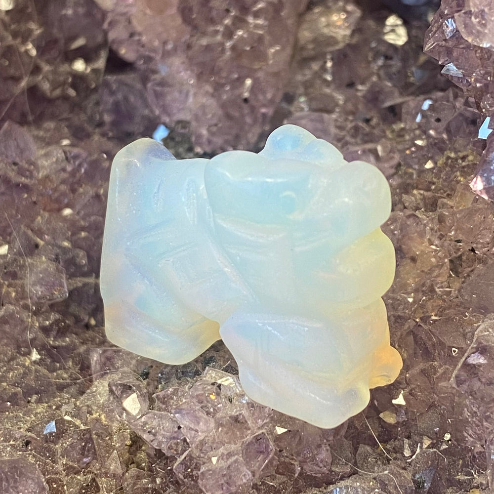 A small Opalite Dragon Carving, placed on a bed of purple crystal points.