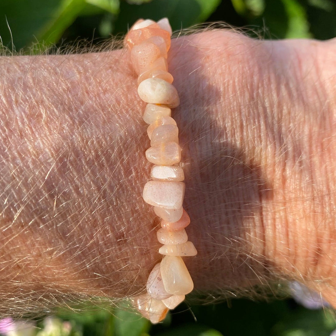 A peach-coloured stone chip bracelet worn on a person's wrist, with a background of green garden foliage.