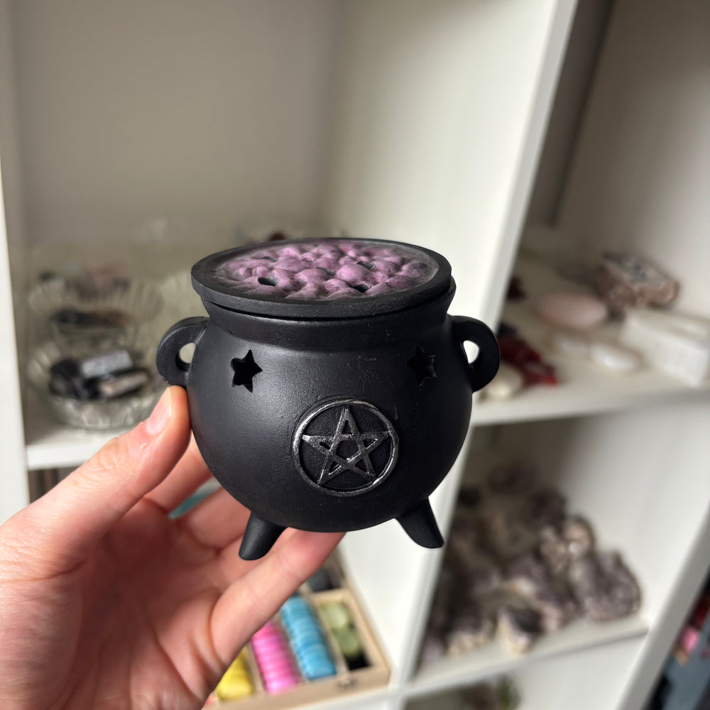 Black ceramic incense burner with purple interior held in a hand against a blurred indoor background.