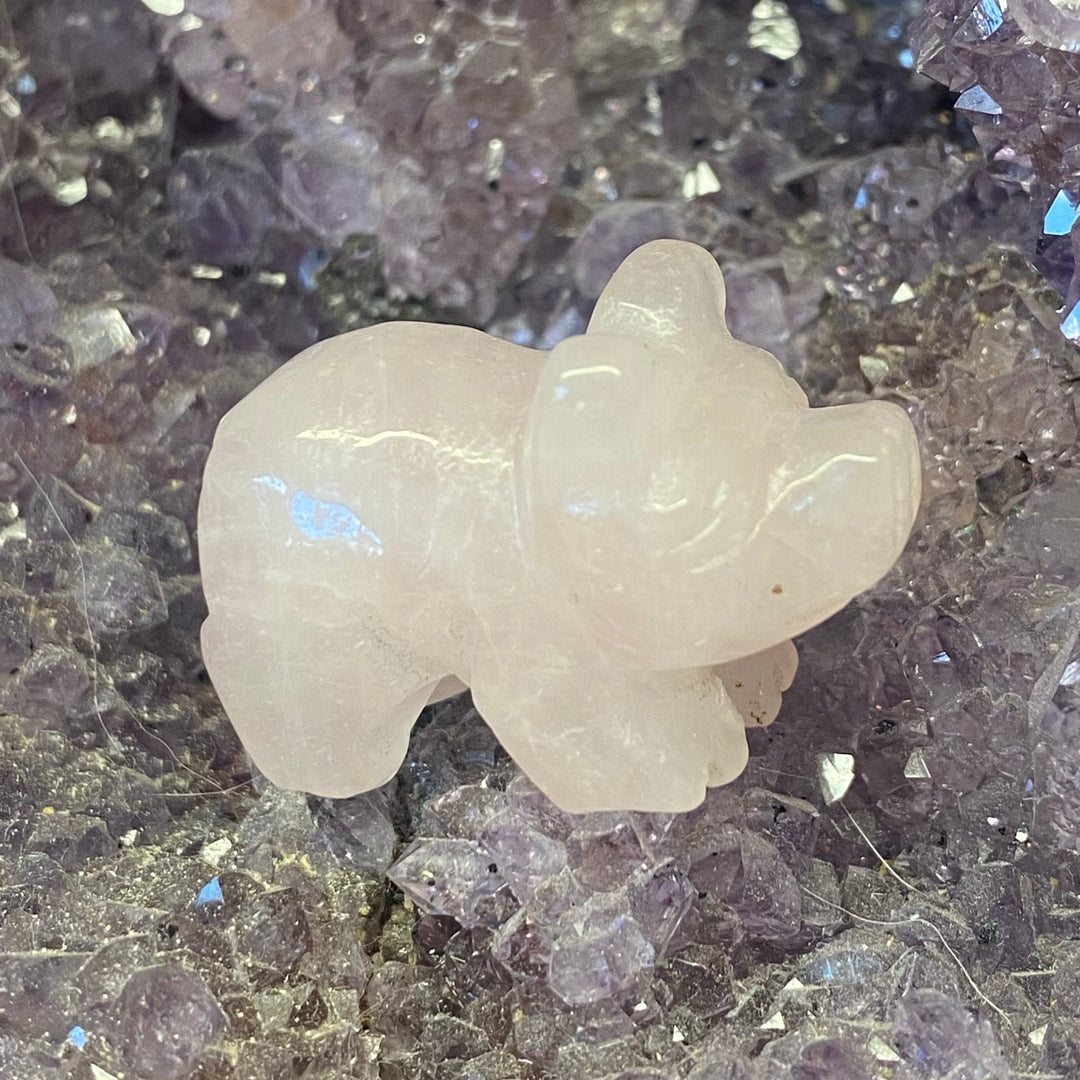 A small Rose Quartz Pig Carving figurine resting on a bed of purple crystal points.