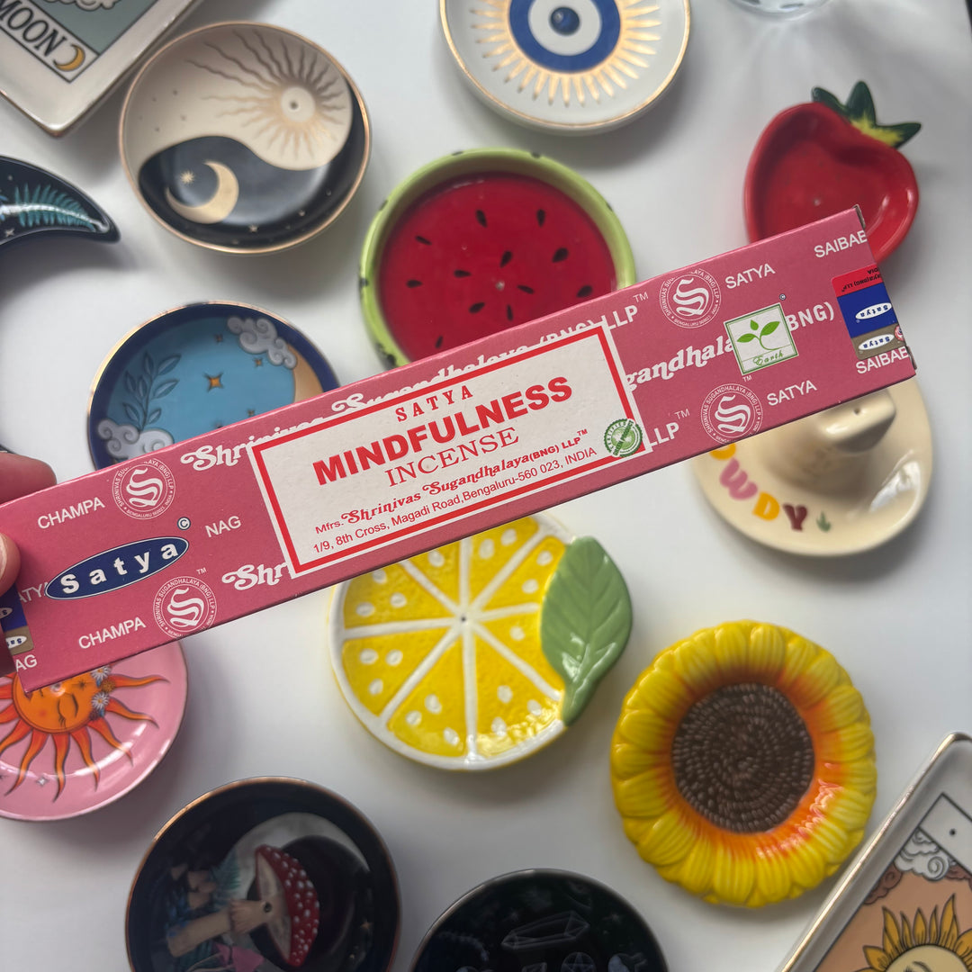 Satya Mindfulness incense stick held over a collection of colourful ceramic plates.