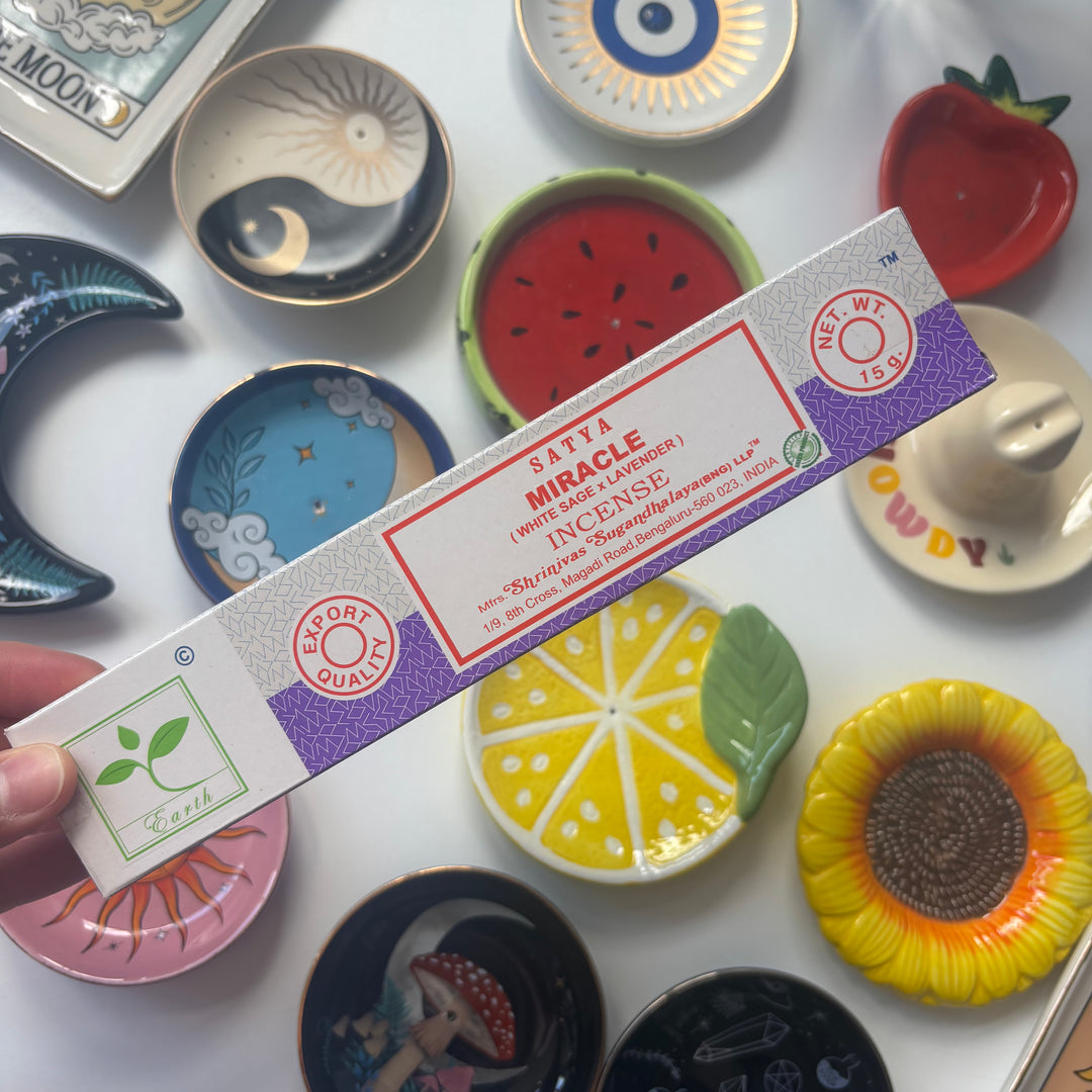 Satya Miracle incense packaging held over a collection of colourful ceramic plates.