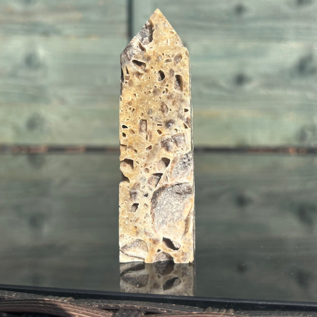 A sphalerite crystal tower displayed on a reflective surface with a wooden background.