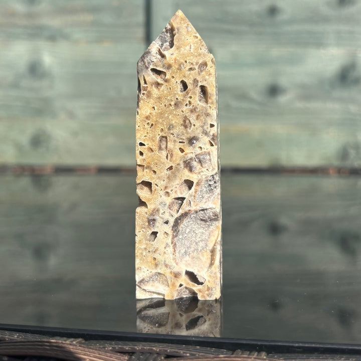 A sphalerite crystal tower displayed on a reflective surface with a wooden background.