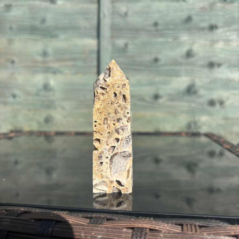 A sphalerite crystal tower displayed on a reflective surface with a wooden background.