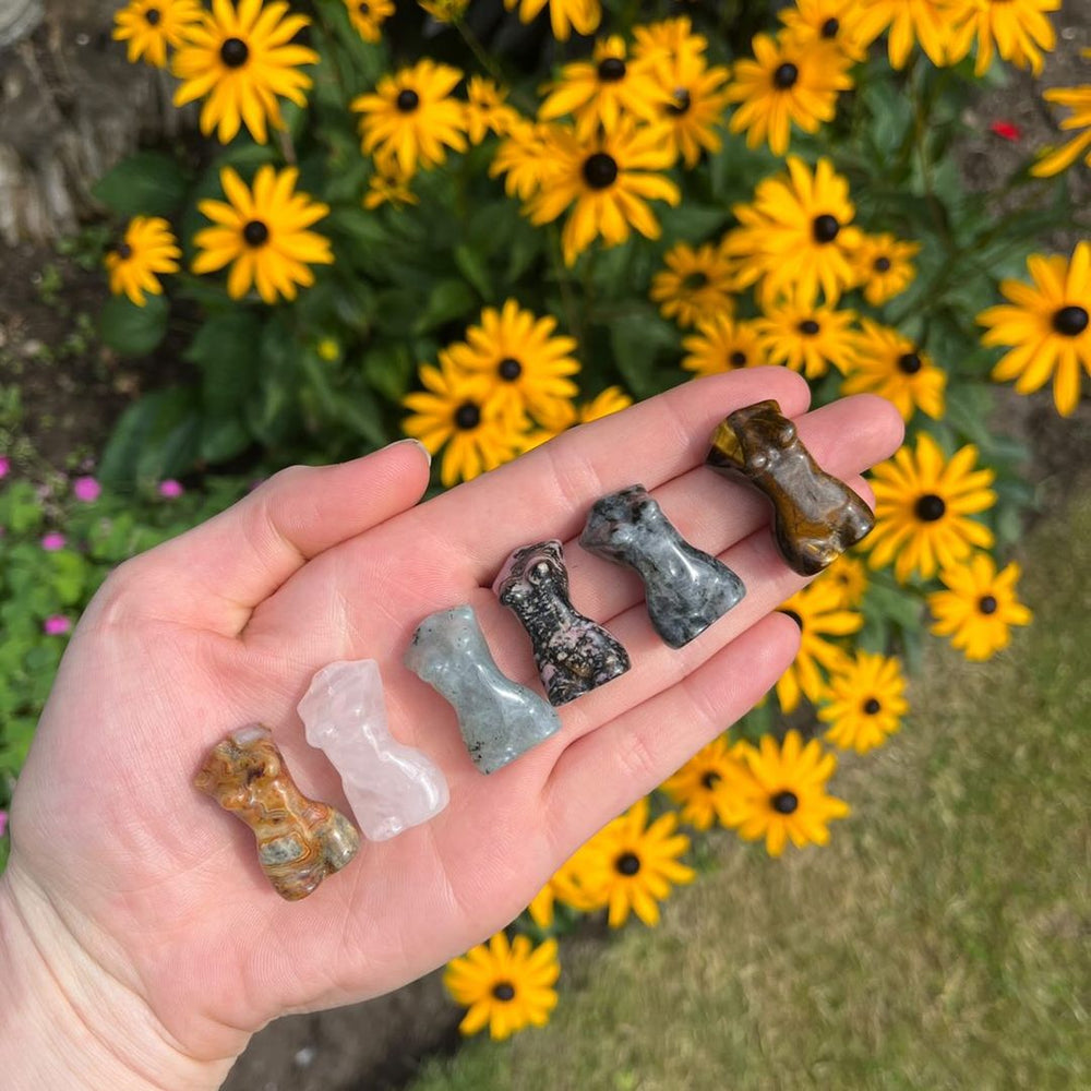 Tiger Eye Goddess Body Crystal Carvings held in a hand in a brightly lit garden 